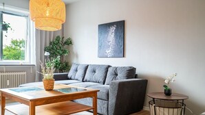 A modern living room with a grey sofa, a wooden coffee table, a hanging light fixture, a framed artwork, and a potted plant.