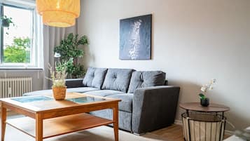 A modern living room with a grey sofa, a wooden coffee table, a hanging light fixture, a framed artwork, and a potted plant.
