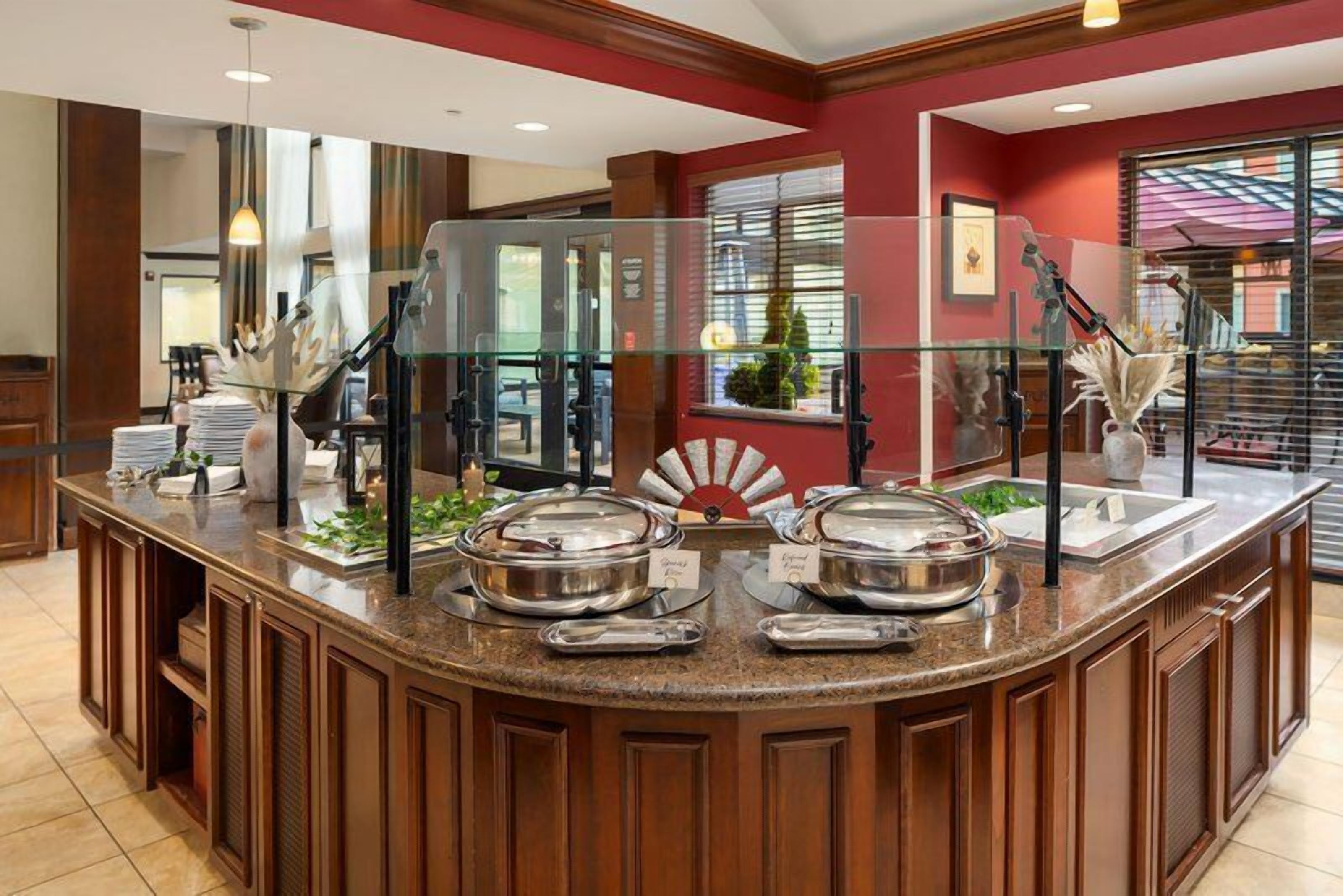 A buffet counter with multiple serving stations, a glass partition, and a view of the hotel lobby.