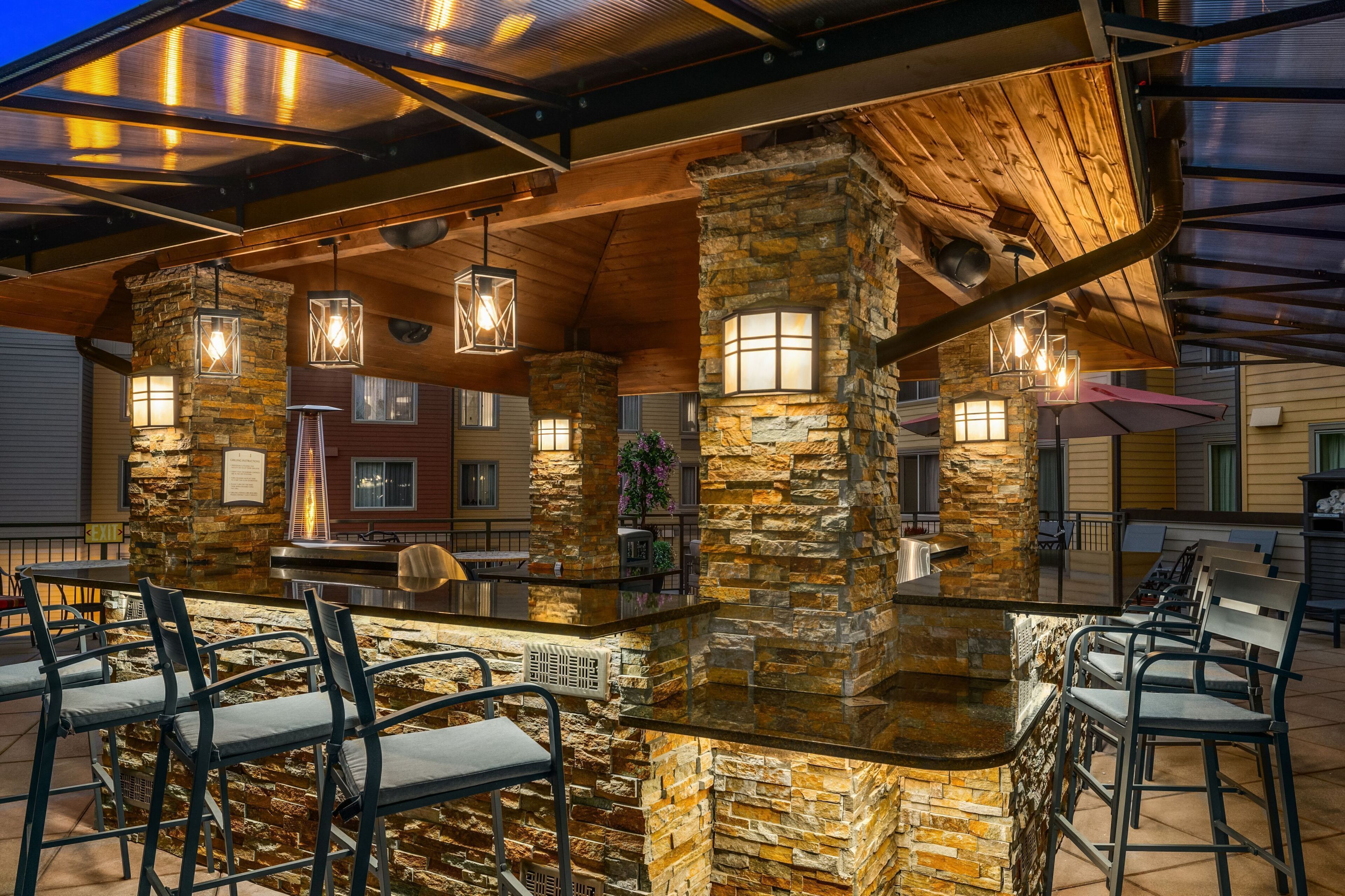An outdoor bar area with stone pillars, hanging lights, and outdoor seating.