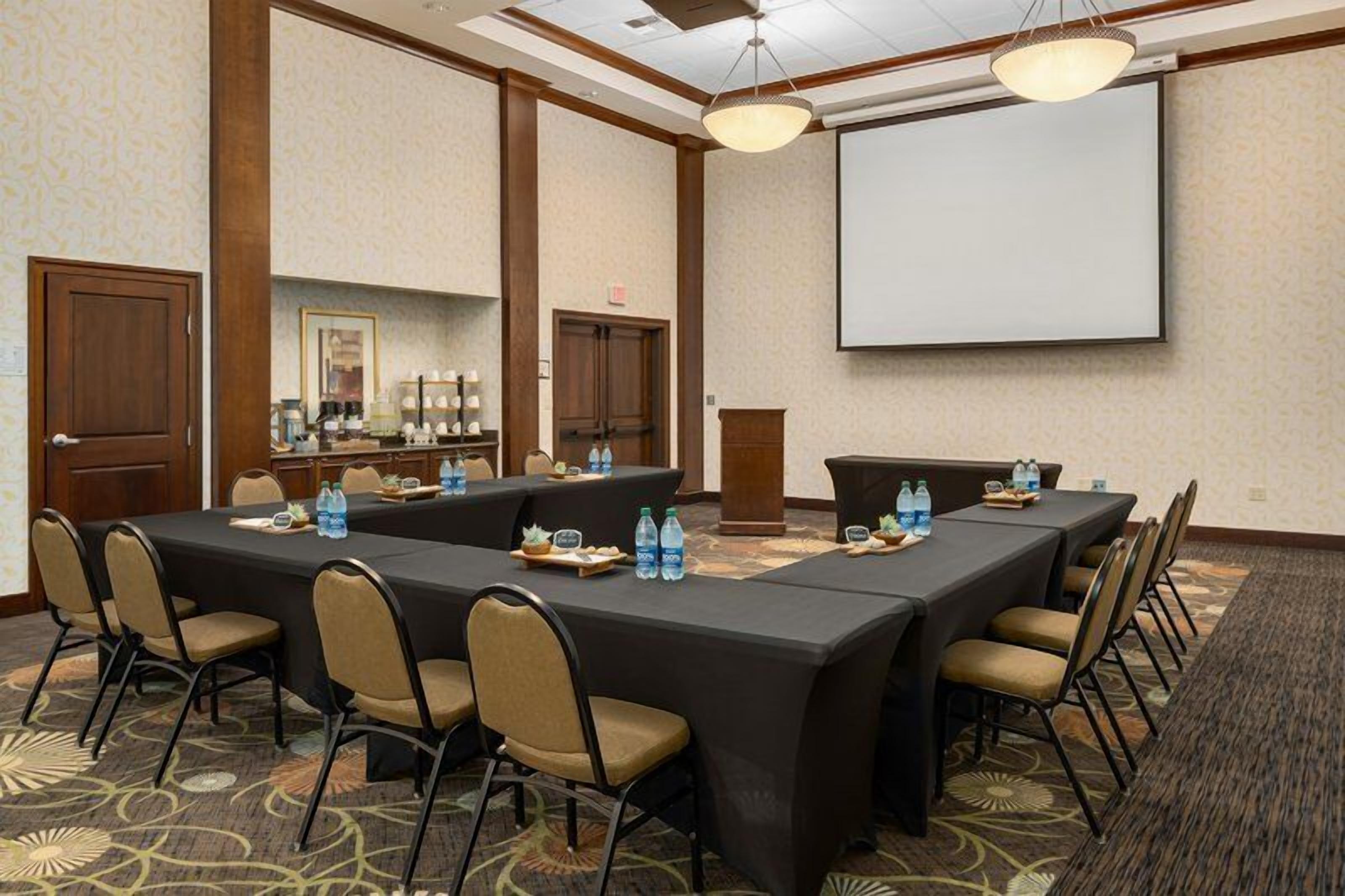 A conference room with a long table, chairs, a projector screen, and a carpeted floor.