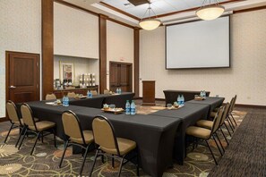 A conference room with a long table, chairs, a projector screen, and a carpeted floor.