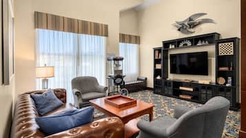 A hotel room with a leather sofa, armchairs, a television, and a bookshelf with various items.