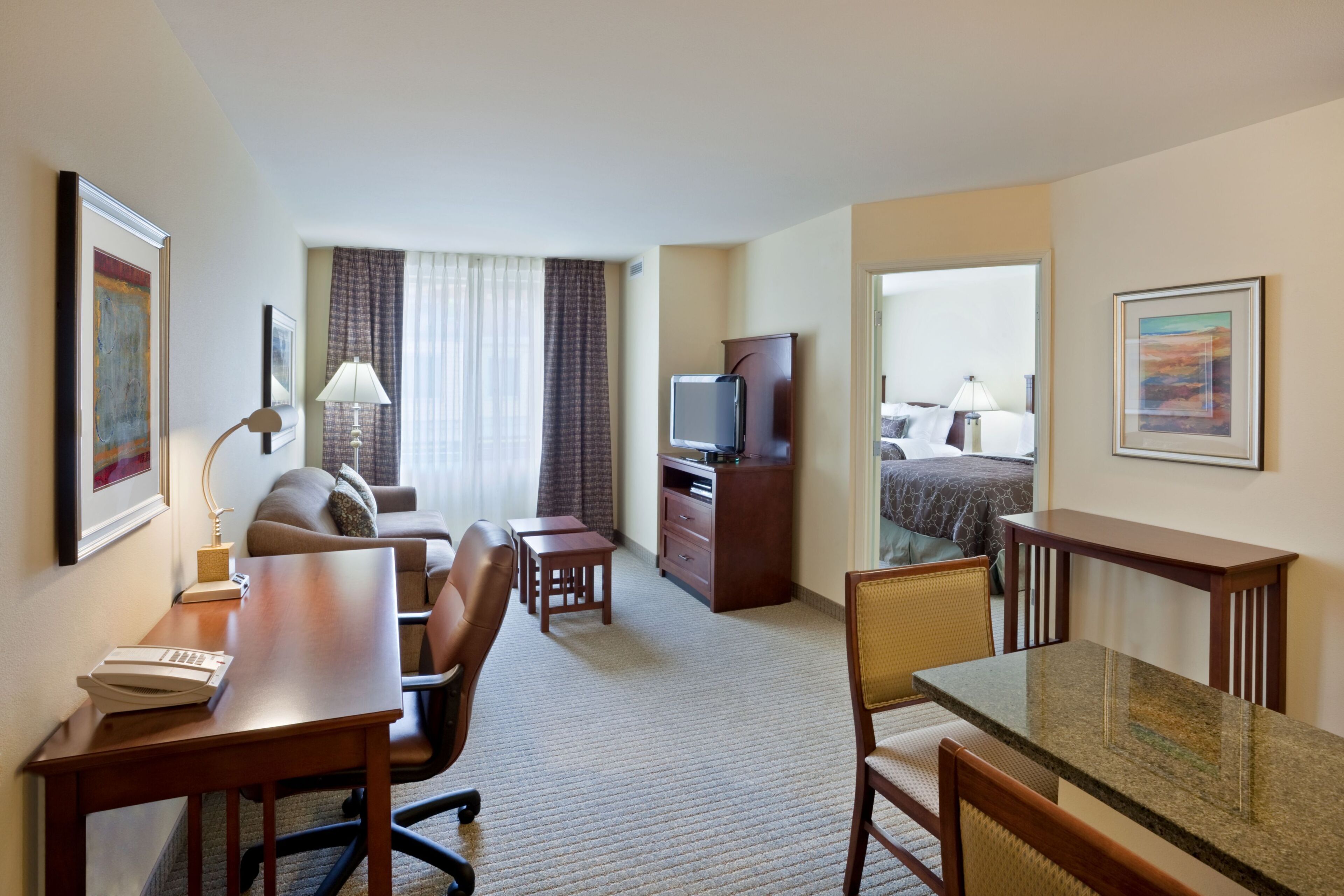 A hotel room with a desk, chair, television, and a bed with a view.