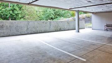 An empty parking garage with concrete floors and walls, a bench, and a covered area with a roof.
