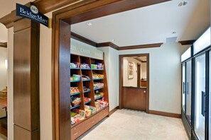A BridgeMart convenience store with shelves stocked with snacks and candy, located in a hallway with wooden trim and a tiled floor.
