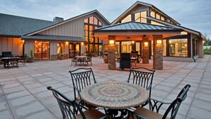 A building with a covered patio area, outdoor seating, and a large windowed entrance.