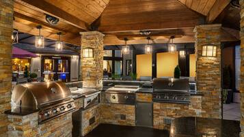An outdoor kitchen with stone pillars, built-in grills, and hanging lights.