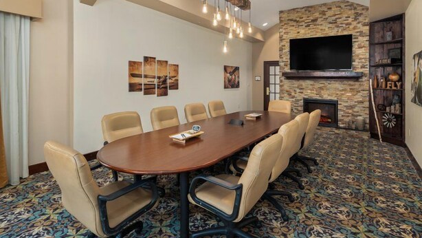 A conference room with a large oval table, six chairs, a fireplace, a flat-screen TV, and a patterned carpet.