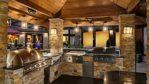 An outdoor kitchen with stone pillars, built-in grills, and hanging lights.