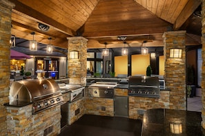 An outdoor kitchen with stone pillars, built-in grills, and hanging lights.