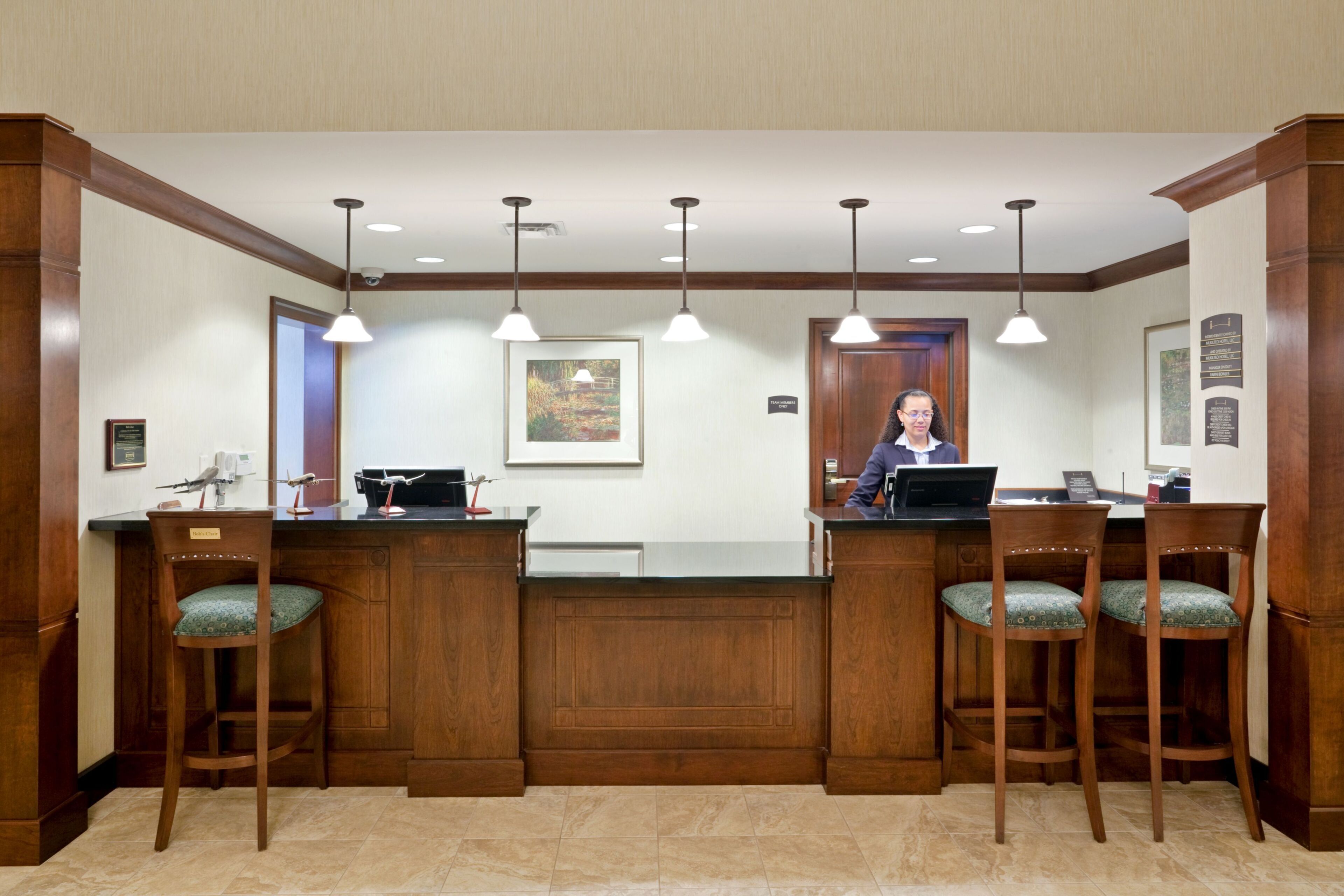 A reception desk with a receptionist, wooden chairs, a framed picture, and a door with a sign.