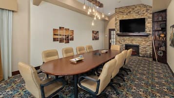 A conference room with a large oval table, six chairs, a fireplace, a flat-screen TV, and a patterned carpet.