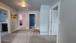 A hallway with carpeted flooring, white walls, and a ceiling light. There are doors leading to other rooms.