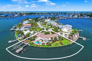 Vue aérienne d’une île résidentielle avec un quai, une piscine et une grande maison.