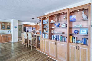 A spacious kitchen with wooden cabinets, a central island, and a dining area with bar stools. - WTFR Home with pool, golf cart, large yard (Indian Rocks Beach)