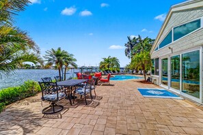 An outdoor pool area with lounge chairs, a dining table, and a view of the water. - WTFR Home with pool, golf cart, large yard (Indian Rocks Beach)