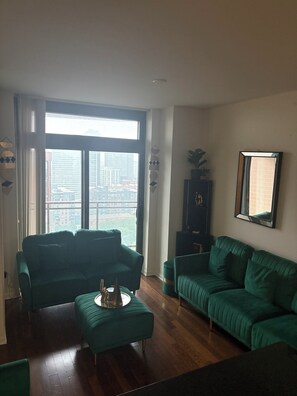 Un salon moderne avec deux canapés verts, une table basse et une grande fenêtre donnant sur la ville.