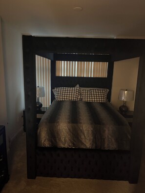A bedroom with a four-poster bed, a nightstand with a lamp, and a window with blinds. - Luxury 1BR Chicago Retreat downtown  Free Parking, Gym, Theater & Patio (Chicago)