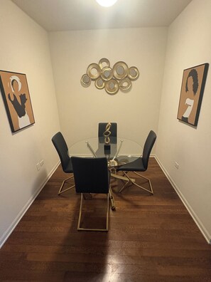A conference room with a glass table surrounded by four chairs, a decorative wall piece above the table, and framed artwork on the walls. - Luxury 1BR Chicago Retreat downtown  Free Parking, Gym, Theater & Patio (Chicago)