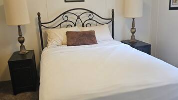 A neatly made bed with white bedding and a brown pillow, flanked by two bedside tables with lamps, in a room with a simple, clean design.