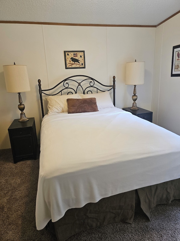 A neatly made bed with white bedding and a brown pillow, flanked by two bedside tables with lamps, in a room with a simple, clean design.
