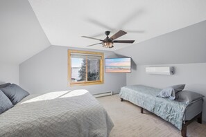 A bedroom with two beds, a ceiling fan, a window with a view, and a wall-mounted air conditioner.