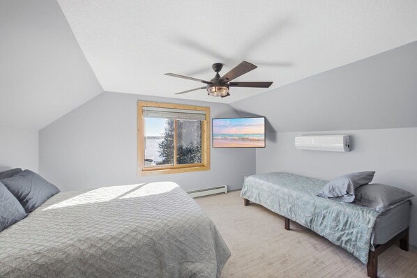 A bedroom with two beds, a ceiling fan, a window with a view, and a wall-mounted air conditioner.