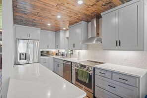 Une cuisine moderne avec des meubles blancs, des appareils électroménagers en acier inoxydable et un plafond en bois.