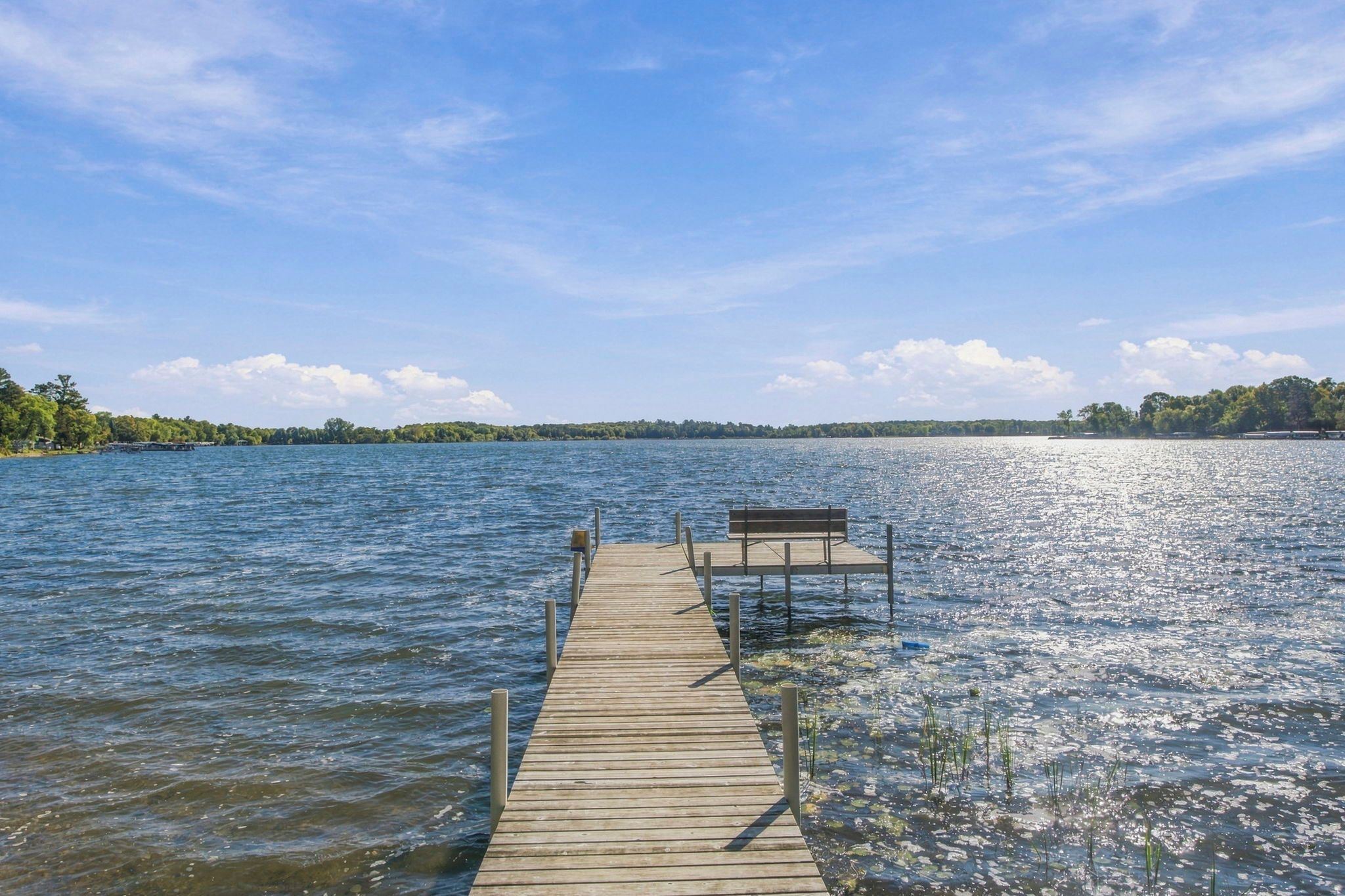 A wooden pier extending into a calm lake with a bench at the end.