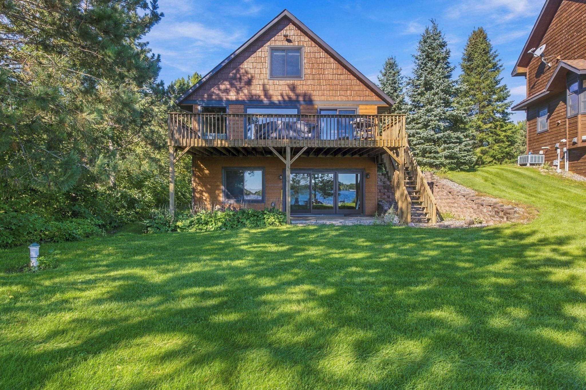 Une maison en bois à deux étages, dotée d’un balcon, entourée d’une pelouse bien entretenue et d’arbres.