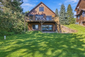 A two-story wooden house with a balcony, surrounded by a well-maintained lawn and trees.