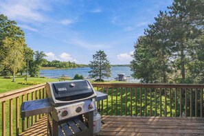 Un barbecue installé sur une terrasse en bois, donnant sur un lac où l’on peut voir des bateaux, des arbres et un ciel dégagé.
