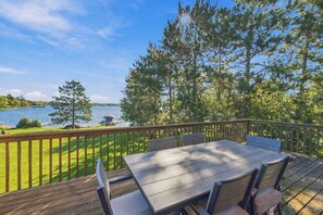 An outdoor deck with a table and chairs, overlooking a lake with a dock and boats.