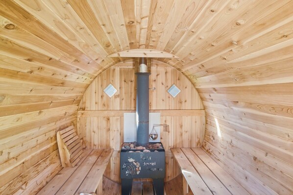 A sauna with wooden walls and benches, a central pillar, and a stone basin.