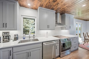 A modern kitchen with grey cabinets, a stainless steel dishwasher, an LG oven, and a window with a view of trees.