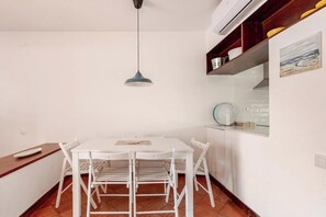 A dining area with a white table and chairs, a pendant light, and a kitchen area with a stove and cabinets. - Balaia Apartment: BEACH and GOLF (Albufeira)