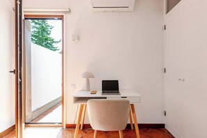 Ein Zimmer mit Schreibtisch, Stuhl und einer offenen Tür, die nach draußen führt.