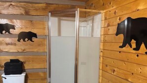 A wooden cabin interior with a glass-enclosed shower, a toilet, and a sink.