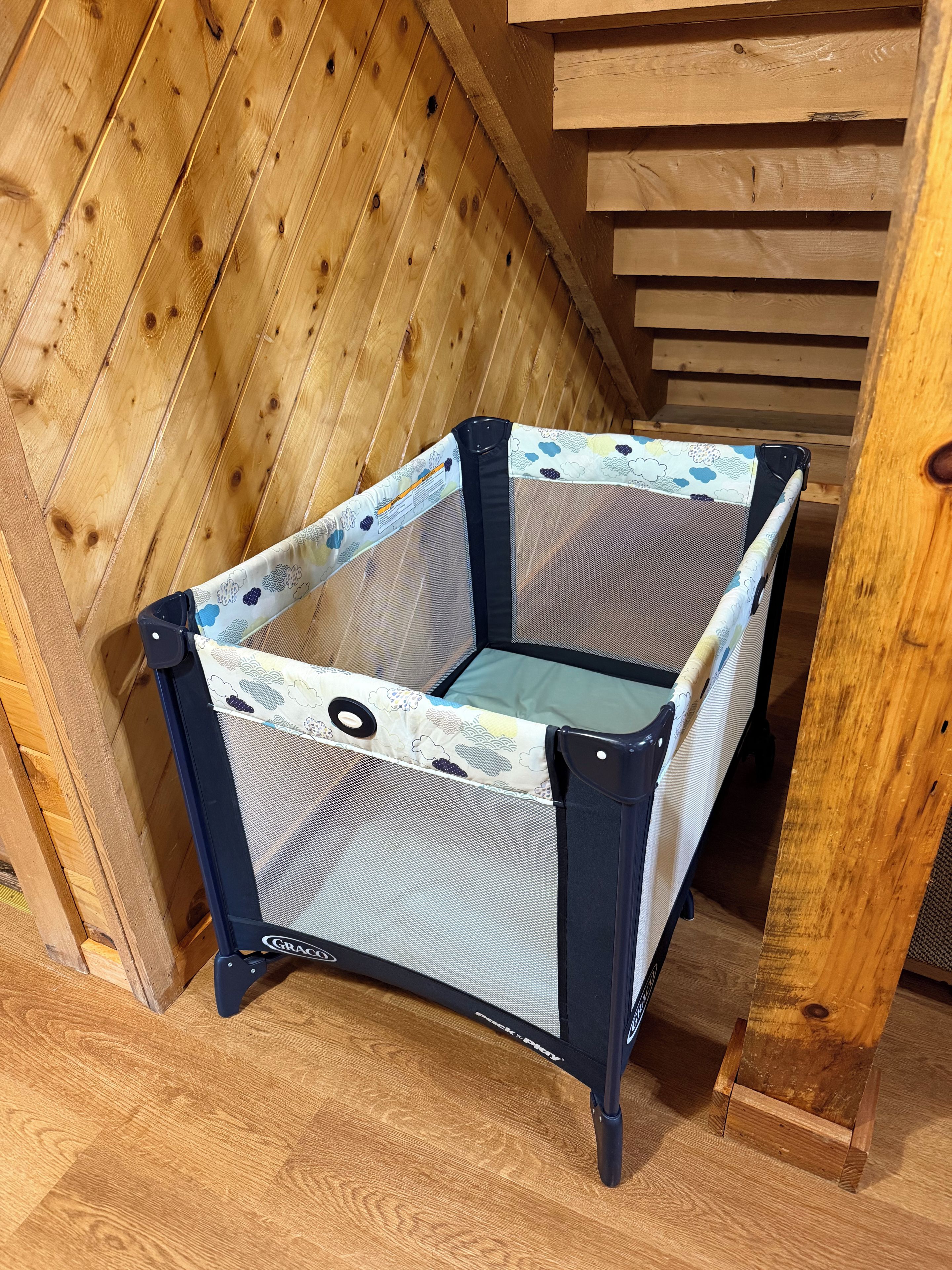 A portable crib with a mesh design and a floral-patterned fabric cover, placed on a wooden floor.