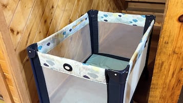 A portable crib with a mesh design and a floral-patterned fabric cover, placed on a wooden floor.