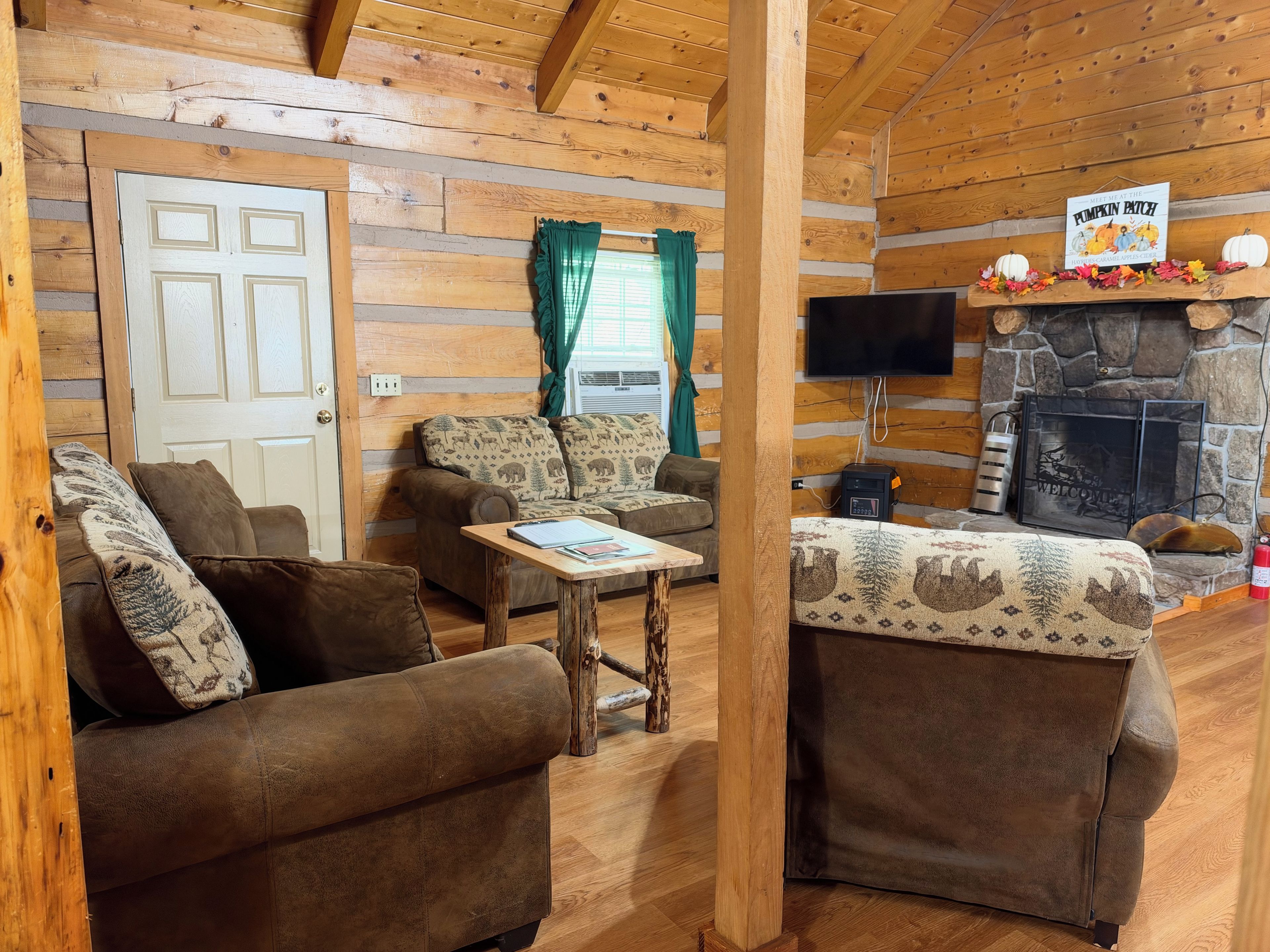A cozy cabin interior with a fireplace, wooden walls, and two sofas.