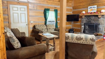 A cozy cabin interior with a fireplace, wooden walls, and two sofas.
