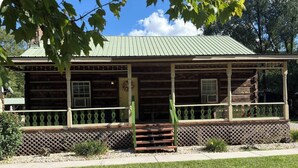 A log cabin with a porch, a front door, and a small staircase leading up to the entrance.