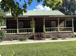 A log cabin with a porch, a front door, and a small staircase leading up to the entrance.