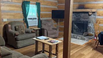 Ein rustikales Blockhaus-Interieur mit Kamin aus Stein, Holzmöbeln und einem Fernseher.
