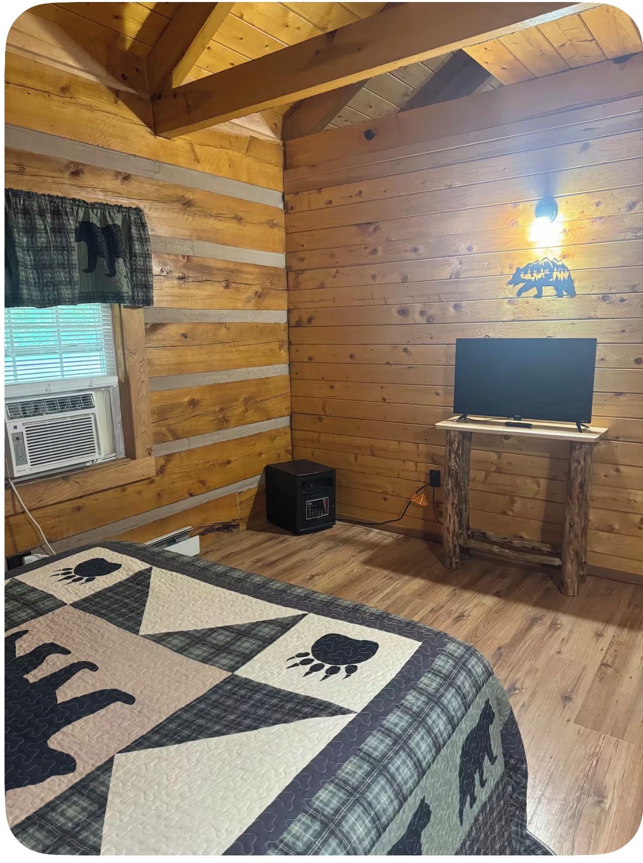 A cozy room with wooden walls, a quilted bed, a television on a wooden stand, and a wall-mounted light.