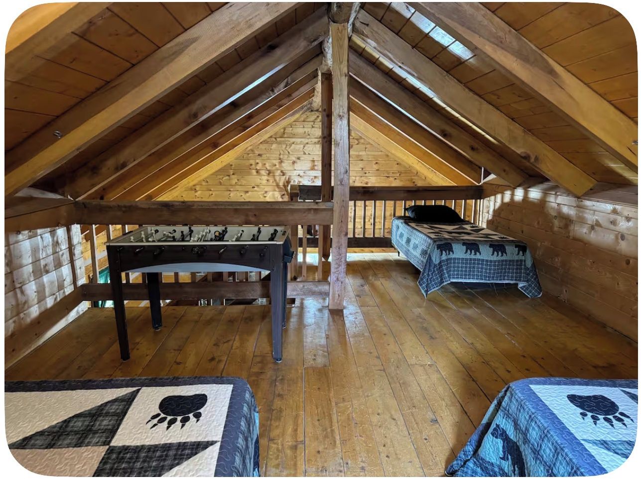 An attic room with wooden beams, a foosball table, and two beds with animal-themed bedding.