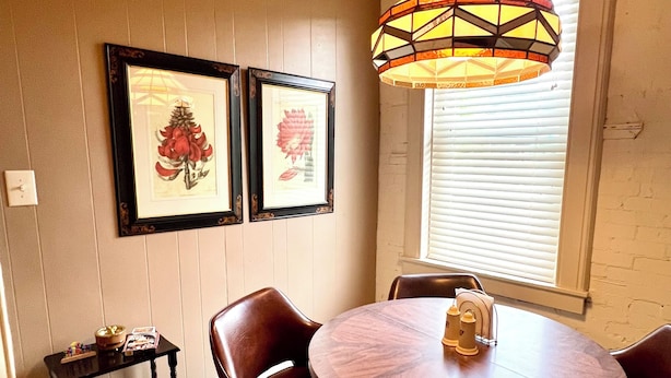 Un comedor con una mesa redonda de madera, cuatro sillas, una mesita auxiliar y un colgante decorativo.