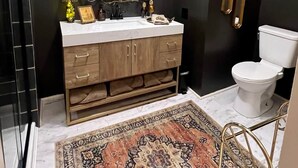 A bathroom with a dark wall, a white sink with a gold frame, a large mirror, and a toilet. - Vulture's Roost (Makanda)